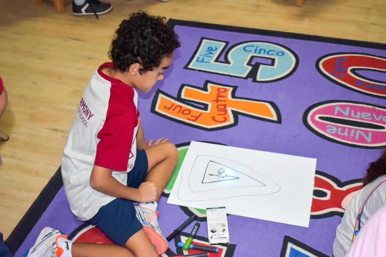 A child from IVY STEM International School engaged in a coloring activity on a colorful educational carpet featuring numbers and Spanish words. The child is focused on a drawing, with markers nearby, indicating an educational setting designed for young children.